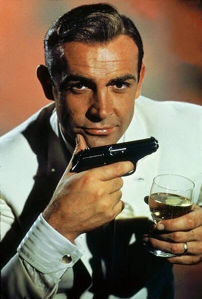 Sean Connery as James Bond in Dr. No holding a gun and a glass of champagne.