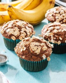 Healthy banana muffins with oatmeal on top and bananas in background