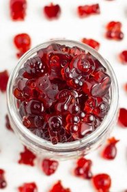 Close-up, overhead view of a glass jar overflowing with bright red tart cherry gummies on a white countertop.