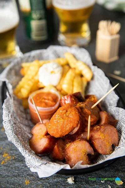 A closer shot of a serving of currywurst, highlighting the sprinkle of curry and dollop of curry ketchup.