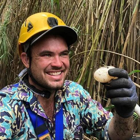 A smiling Chris 'Willow' Wilson, holding a crocodile egg and wearing a hard hat.