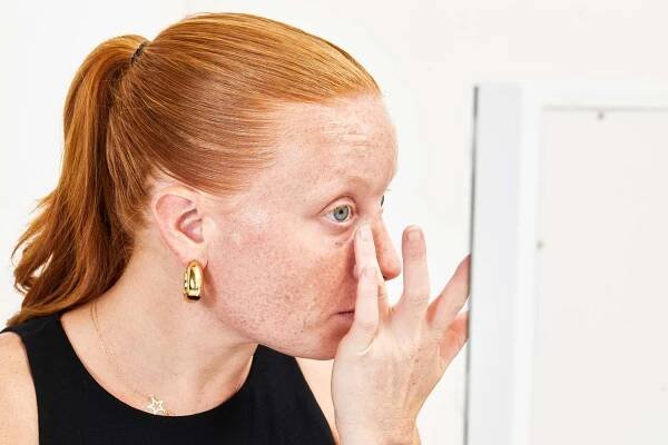 Closeup of hand applying anti-aging eye tightening serum under person’s eye while looking into mirror