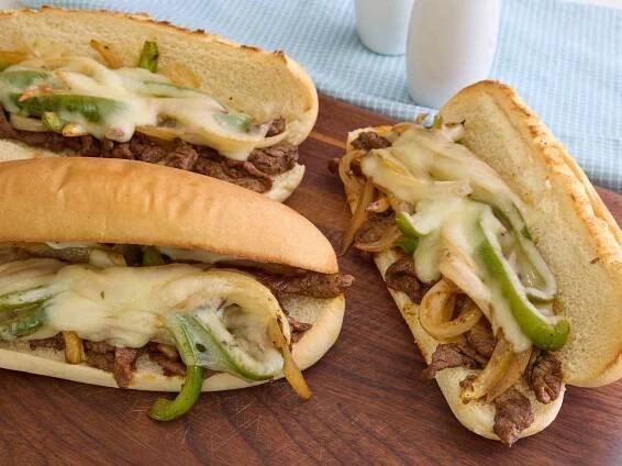 A platter with three Philly cheesesteak sandwiches, topped with melted cheese