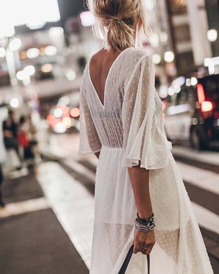 Woman in a white dress walking on a city street at night.