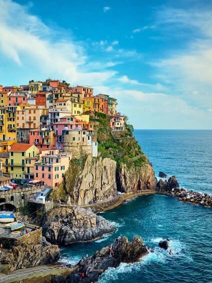 Travel to Italy - Colorful cliffside houses overlooking the sea in Manarola, Cinque Terre, Italy, with a bright blue sky.