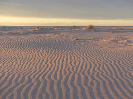 A widely-spread sandy beach with some grass tufts in the far end.