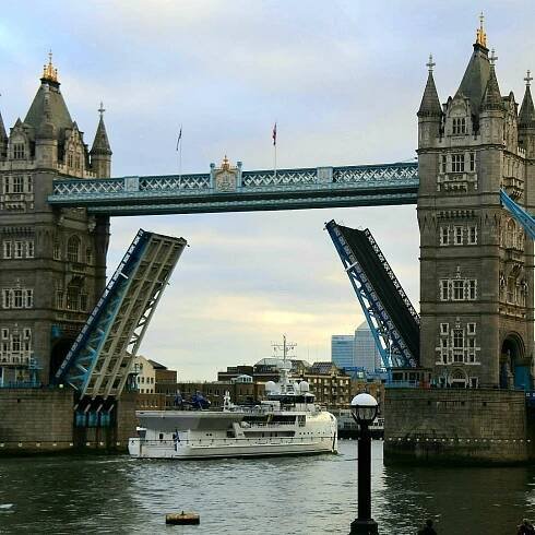 A white yatch passes through the Tower Bridge as the Tower Bridge opens its bascules