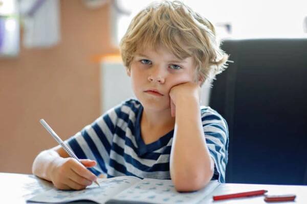 portrait of tired upset boy doing homework in kitchen at home. elementary school studing writing and learning. sad and angry child. - dysgrafie - stock snímky, obrázky a fotky