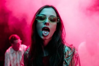 Krásná dívka v slunečních brýlích s LSD na jazyku v nočním klubu s růžovým kouřem — Stock obrázek