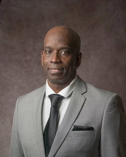 Professional headshot of businessman in gray suit and tie against neutral background.