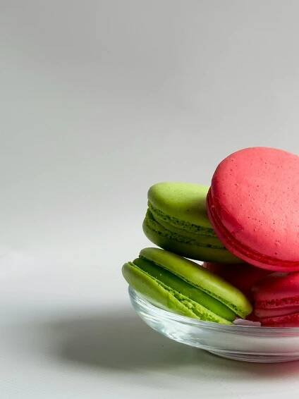 bezplatná Zářivé zelené a růžové macarons naskládané ve skleněné misce na minimalistickém bílém pozadí. Základová fotografie