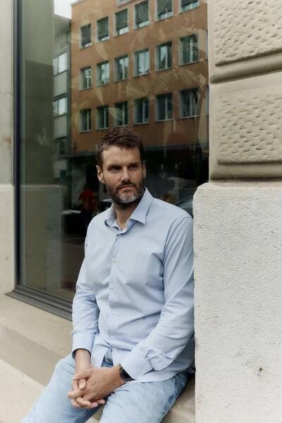 Philippe Reinhardt sitzt im Restaurant Sento in Zürich, trägt ein hellblaues Hemd und Jeans, mit nachdenklichem Blick nach draussen schauend.