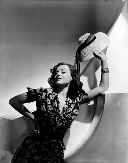 Actress Paulette Goddard wearing a floral-print crepe dress with fan pleating across the bodice and a slope-brimmed knotted-straw hat