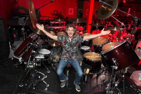 Simon Phillips sitting in front of his drum kit with his arms spread out