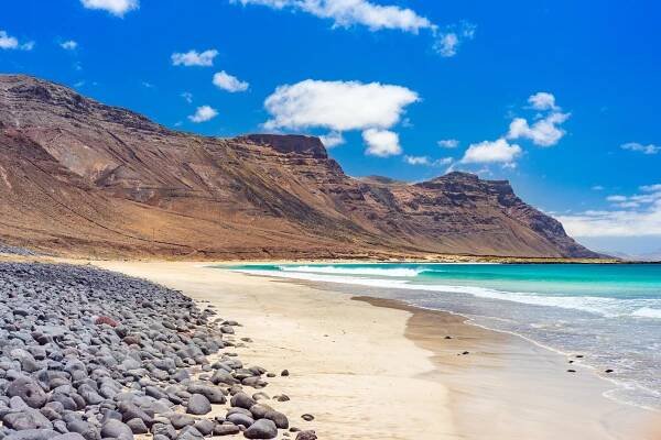 a beach with rocks and mountains in the background