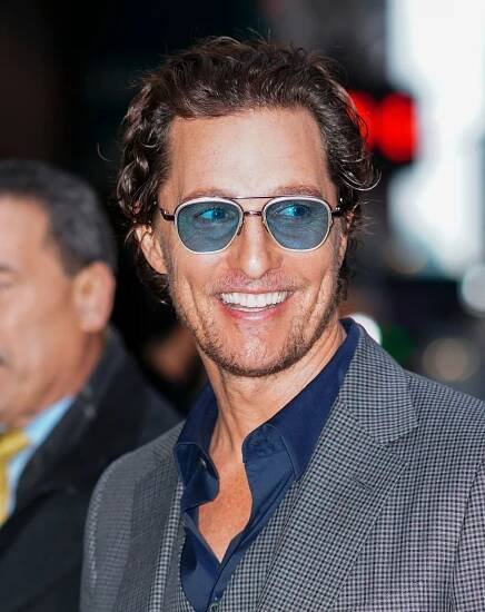 Matthew McConaughey in sunglasses and a checked suit with a blue shirt, smiling at an event