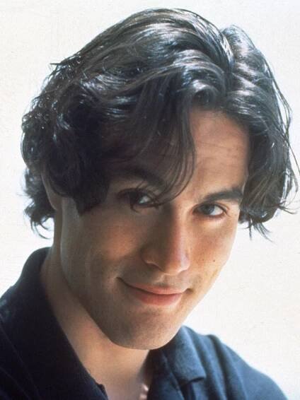 a close up of a person wearing a black shirt and looking at the camera with a smile on his face
