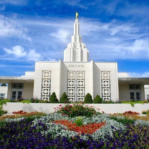 Temple with intricate architecture and a golden statue on top, surrounded by colorful flower gardens under a partly cloudy sky