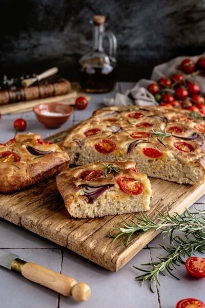 several slices of pizza sitting on top of a wooden cutting board next to tomatoes and herbs