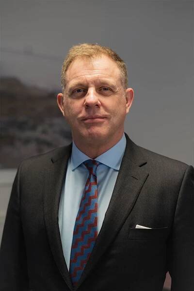 Man standing in suit wearing a blue short and blue/red tie.