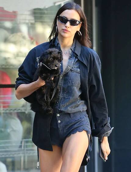 Irina Shayk wears denim short and shirt with fringe knee-high boots while carrying her dog in New York City.
