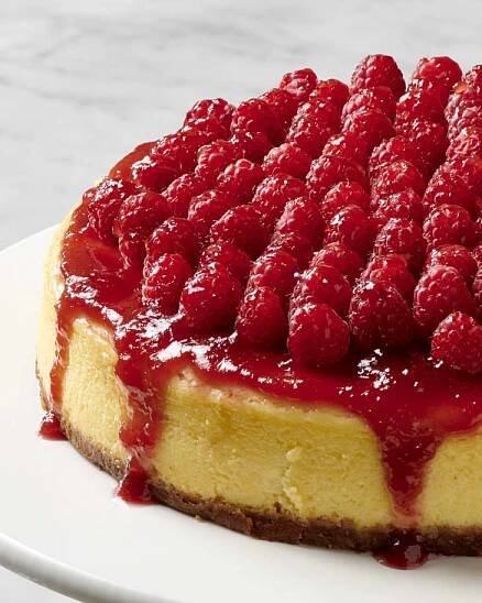 a cheesecake topped with raspberry jam and fresh raspberries on a cake stand
