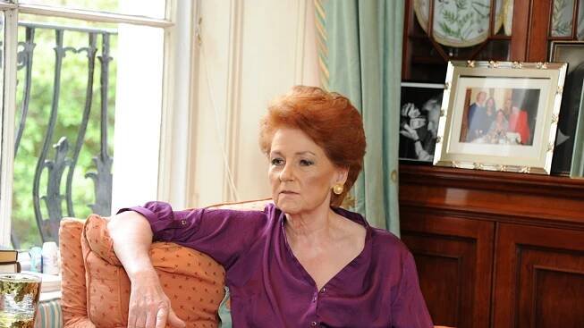 Lady Elizabeth Anson wearing a purple dress and sitting down on a couch looking pensive.