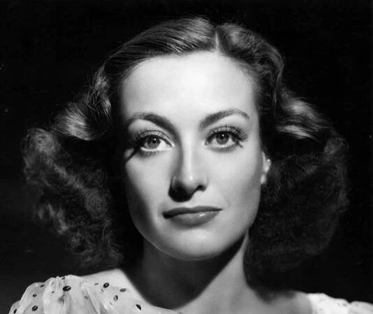 Joan Crawford smiling and looking at camera on black background - 1936