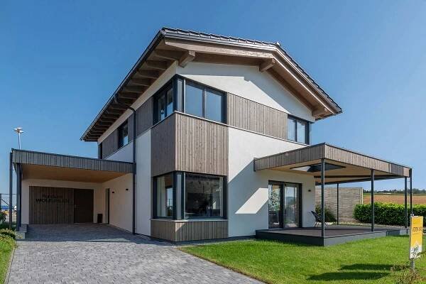 Moderner Fertighausbau von WOLF Haus, Modell Viden 141, mit klaren Linien, Holzelementen und großen Fenstern, umgeben von gepflegtem Rasen und blauen Himmel.
