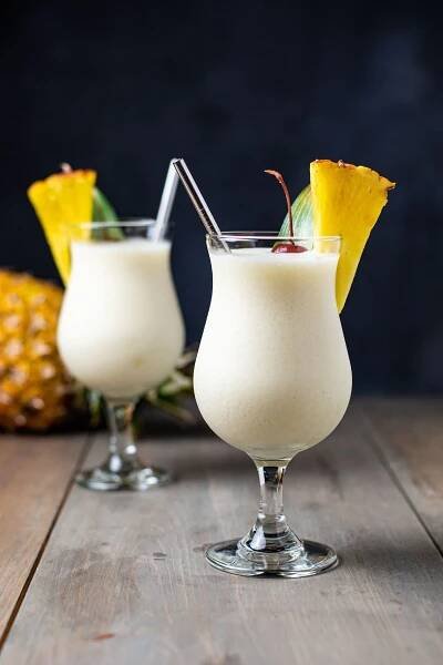 Two frozen Piña Coladas on a wooden table garnished with a pineapple wedge and cherry.