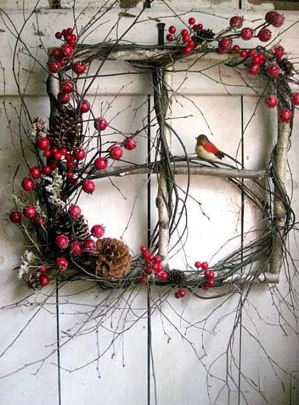 a wreath made out of branches and berries with a bird on the branch next to it